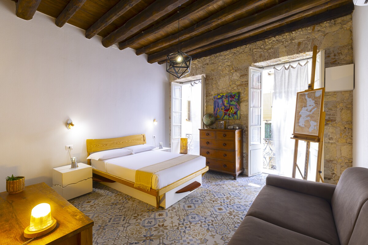 A Sardinian-style bedroom with exposed beams, stone walls and a majolica floor