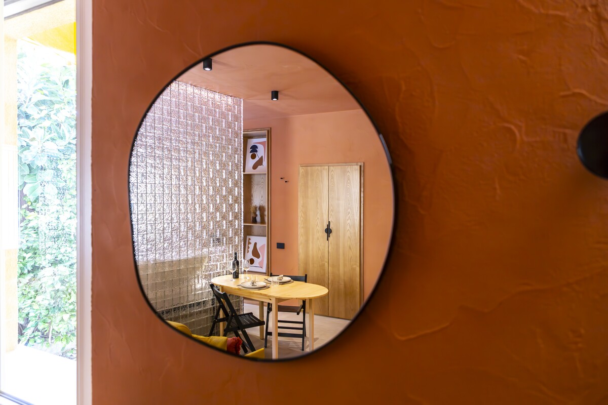 A round mirror on a terracotta wall reflecting the dining room, Propertize apartment in Cagliari