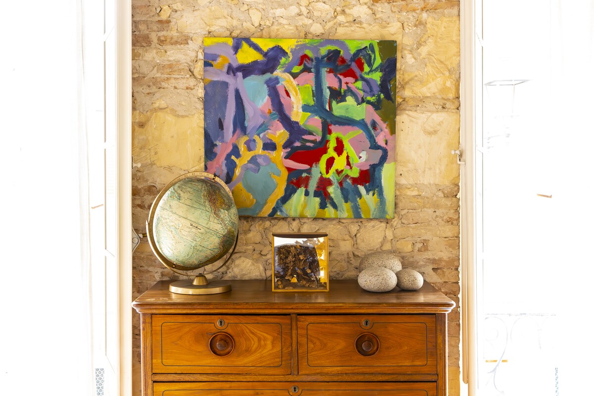 A decorative detail: a colourful painting, a globe and an antique chest of drawers against a stone wall