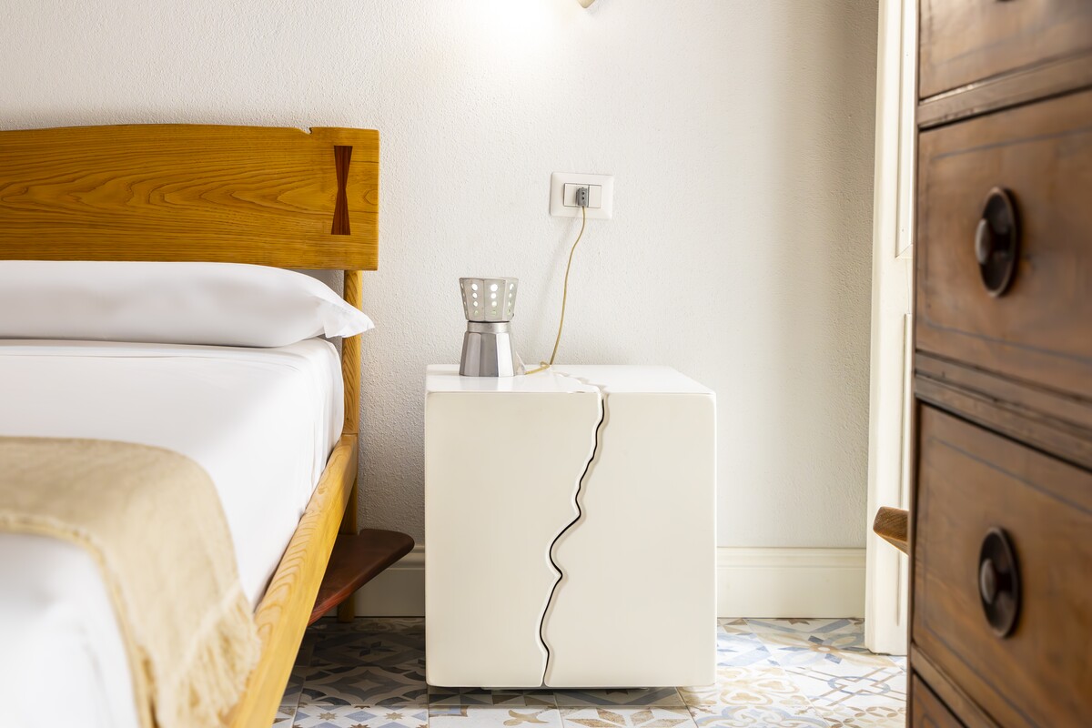 A design bedside table with a moka pot beside the wooden bed on a Sardinian majolica floor